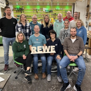 Das Führungskräfteteam von Rewe hat sich im Schreiner-Workshop Holzaufsteller mit dem Firmennamen geschreinert