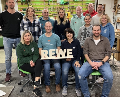 Das Führungskräfteteam von Rewe hat sich im Schreiner-Workshop Holzaufsteller mit dem Firmennamen geschreinert
