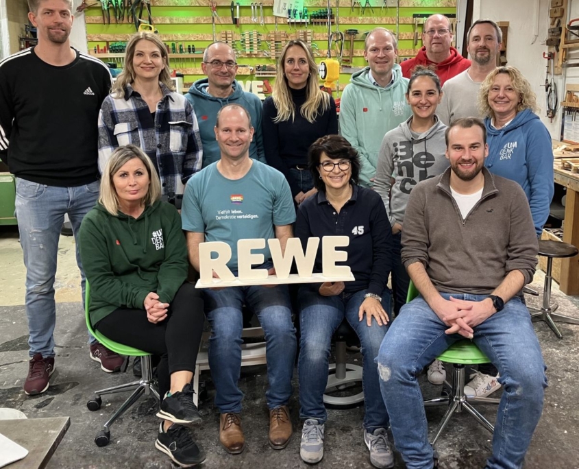 Das Führungskräfteteam von Rewe hat sich im Schreiner-Workshop Holzaufsteller mit dem Firmennamen geschreinert