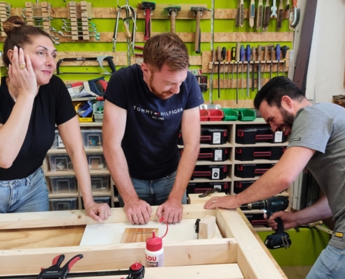 Firmenteam sitzt gemeinsam an selbstgebautem Holztisch nach Schreiner-Workshop