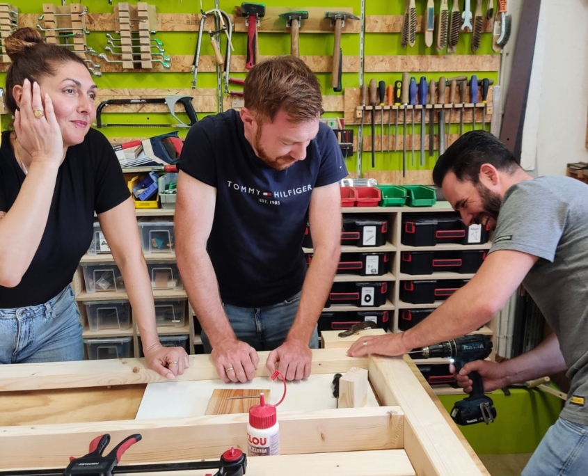 Firmenteam sitzt gemeinsam an selbstgebautem Holztisch nach Schreiner-Workshop