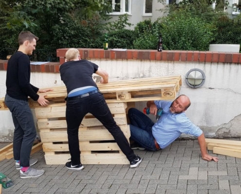 Mitarbeiter bauen gemeinsam Palettenmöbel beim Teambuilding-Event