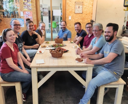 Firmenteam sitzt gemeinsam an selbstgebautem Holztisch nach Schreiner-Workshop